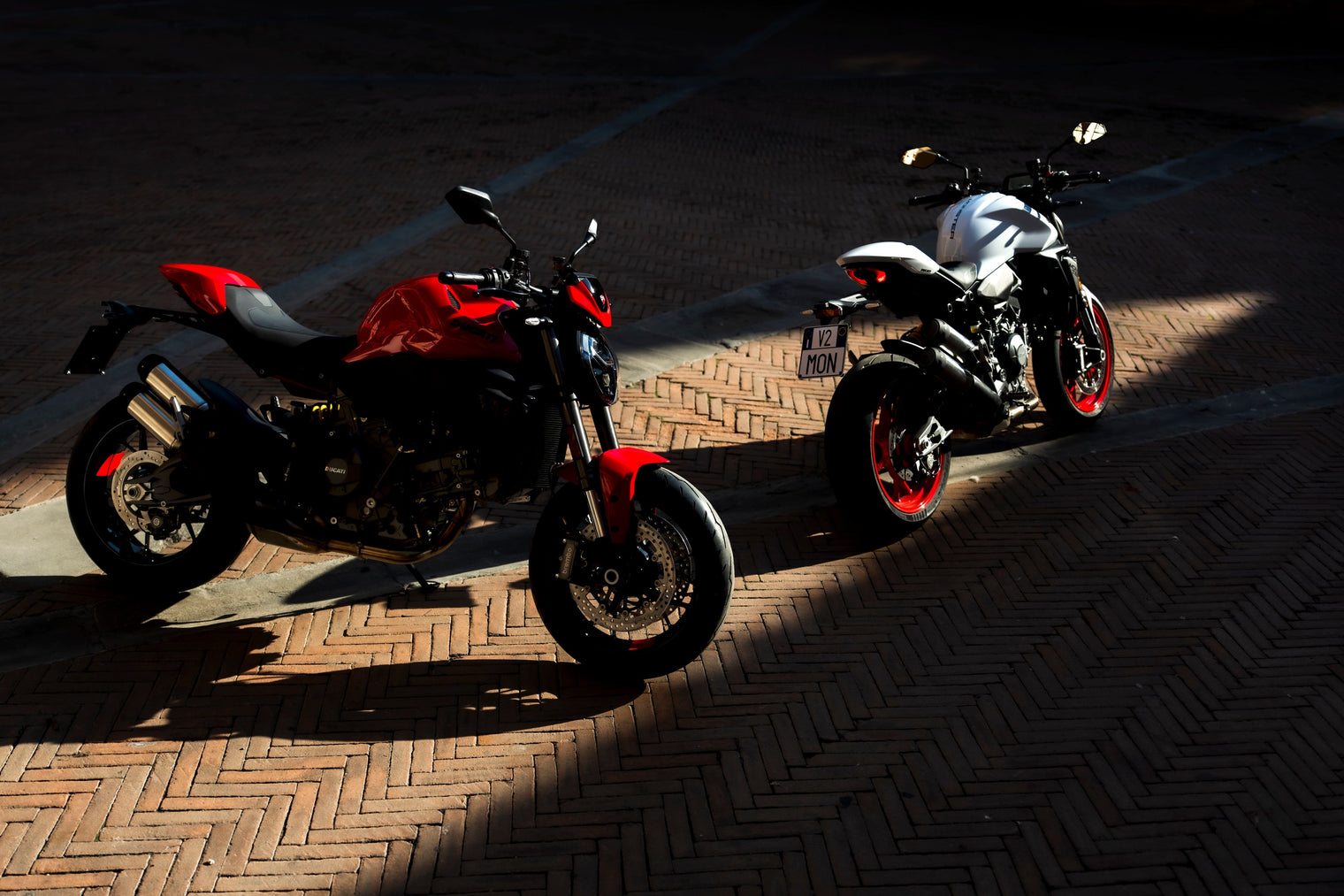 Two 2026 Ducati Monster's, one red and one white sitting on sun streaked pavement